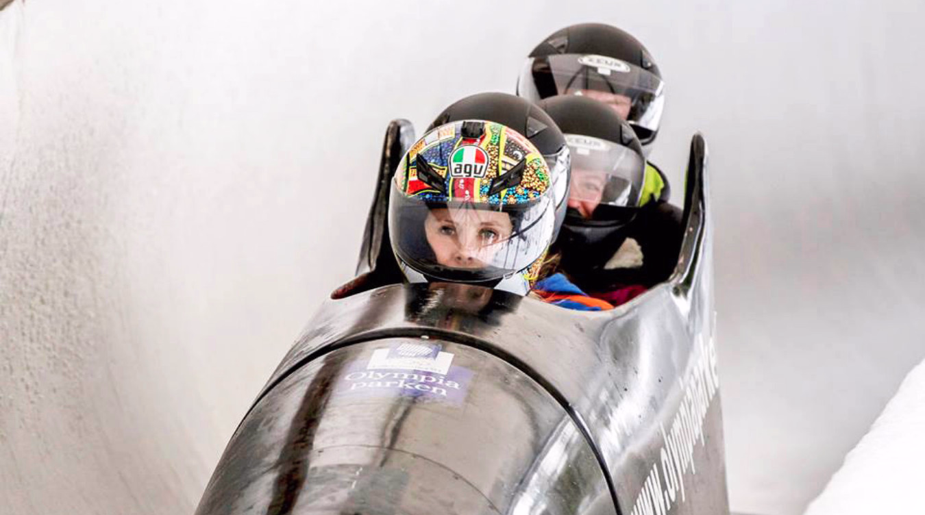 Tre personer i en svart bobsleigh med teksten Olympia park på en isbane