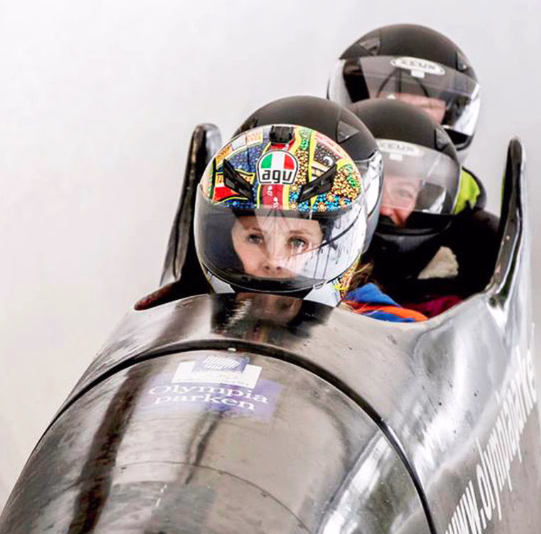 Tre personer i en svart bobsleigh med teksten Olympia park på en isbane