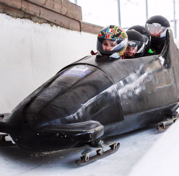 Tre personer i en svart bobslede kjører gjennom en sving på en islagt bane