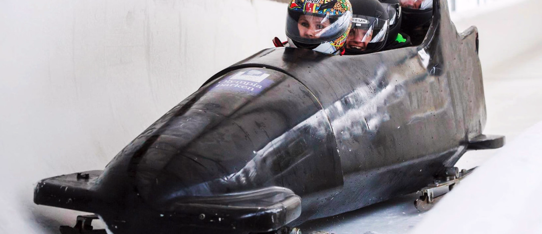 Tre personer i en svart bobslede kjører gjennom en sving på en islagt bane