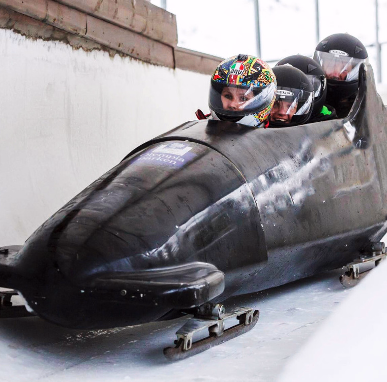 Tre personer i en svart bobslede kjører gjennom en sving på en islagt bane