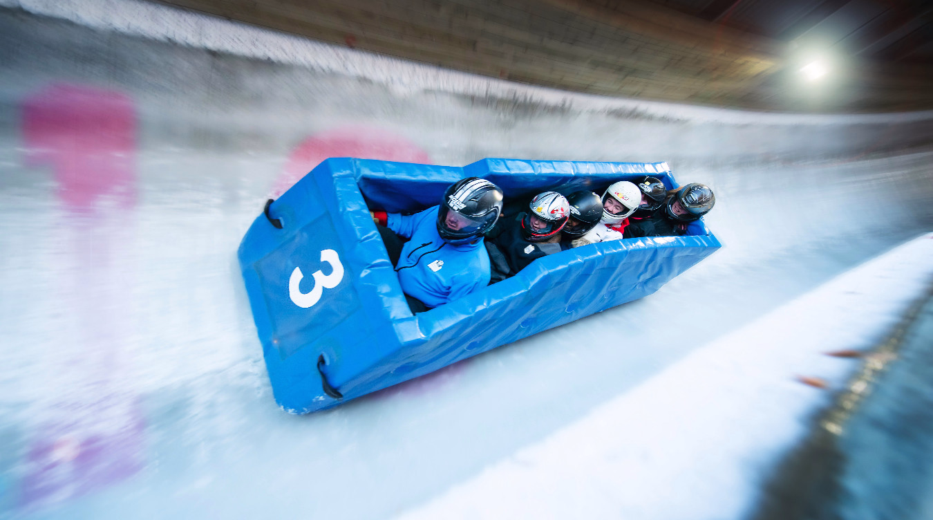 Fire personer med hjelm kjører en blå bobslede med tallet 3 på en isbane