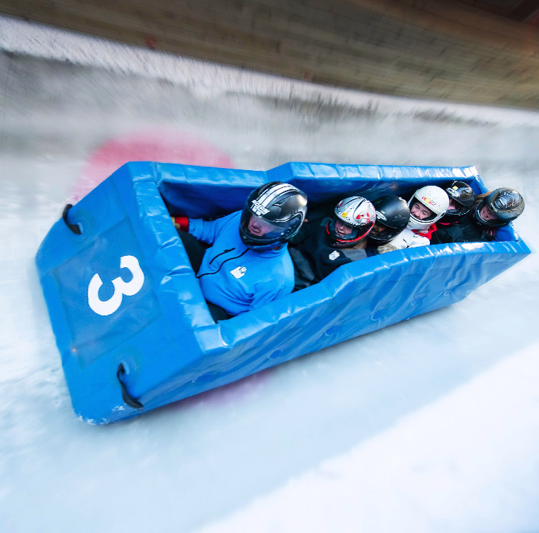 Fire personer med hjelm kjører en blå bobslede med tallet 3 på en isbane