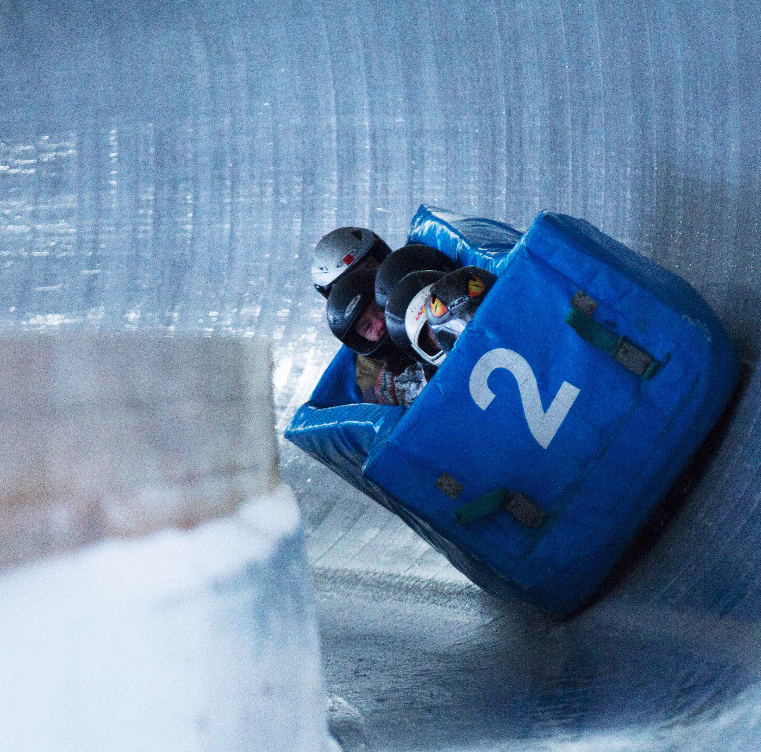 Blå bobslede med nummer 2 og utøvere i hjelm i en sving på en isbane