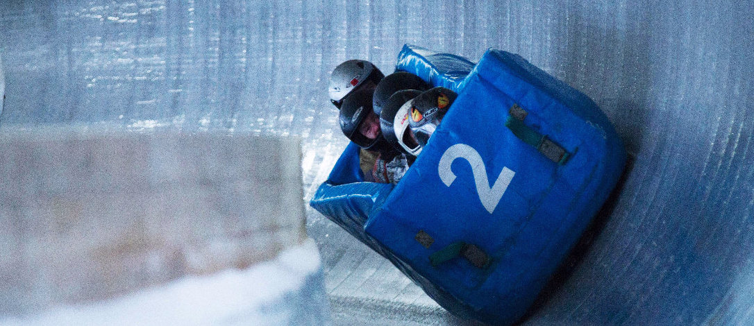 Blå bobslede med nummer 2 og utøvere i hjelm i en sving på en isbane