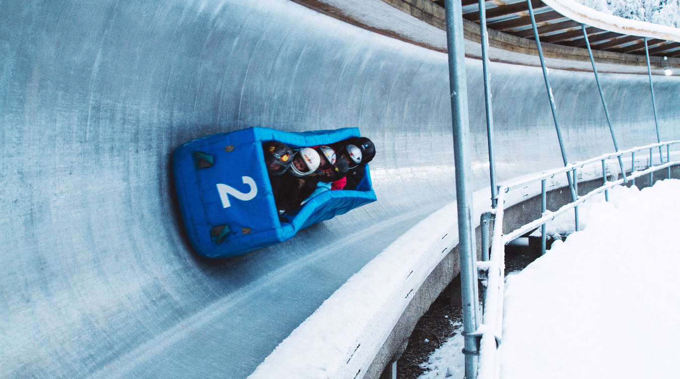 Blå bobslede med tallet 2 og fire personer som kjører ned en isete bane i snøen