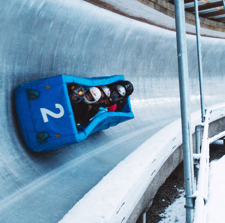 Blå bobslede med tallet 2 og fire personer som kjører ned en isete bane i snøen