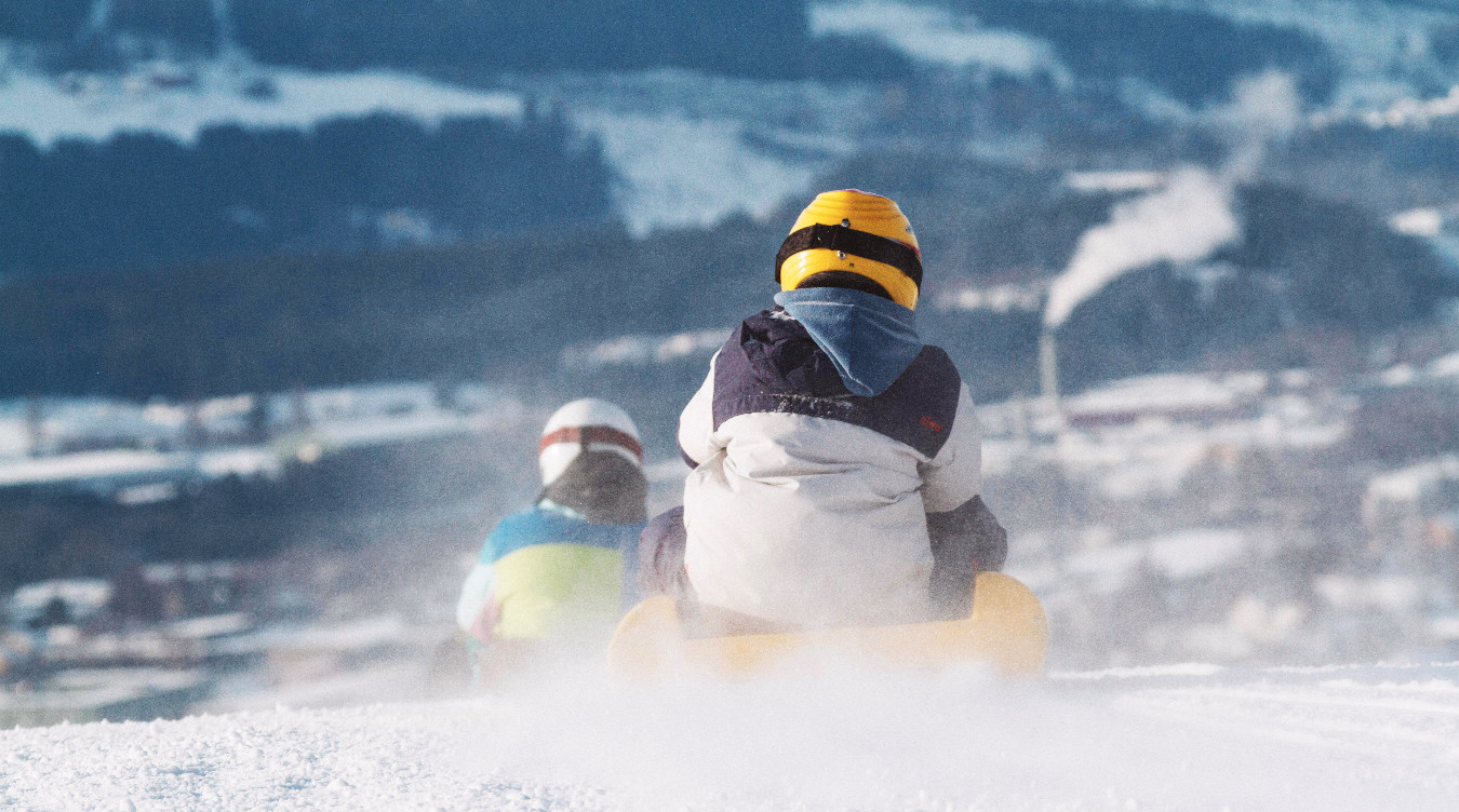 To personer aker ned en snøbakke med snøsprut rundt seg