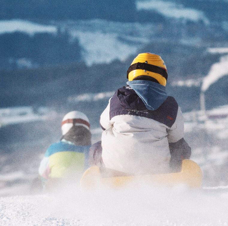 To personer aker ned en snøbakke med snøsprut rundt seg