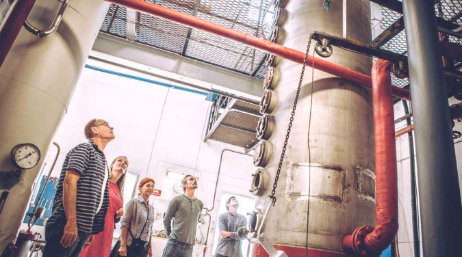 Fem personer i et industrianlegg ser på en stor metallsøyle med rør og målere