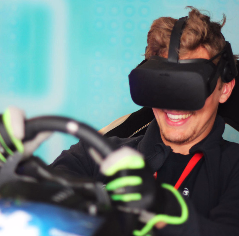 Smilende person med VR-headset i et racingsete som holder et ratt