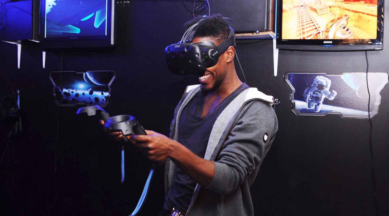 Person med VR-briller og kontrollere smiler i et rom med skjermer og romfartstema
