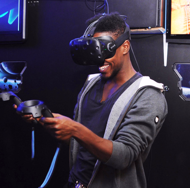 Person med VR-briller og kontrollere smiler i et rom med skjermer og romfartstema