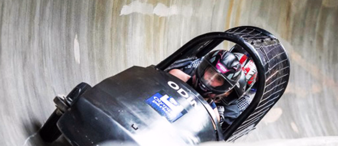 To personer i en svart bobslede med teksten ODIN på en isbane