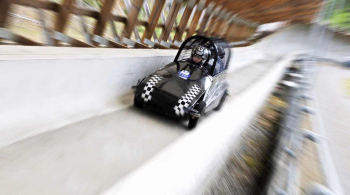 Svart gokart med sjakkmønster og person med hjelm i fart på en bane