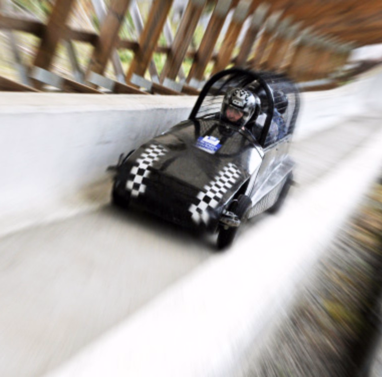 Svart gokart med sjakkmønster og person med hjelm i fart på en bane