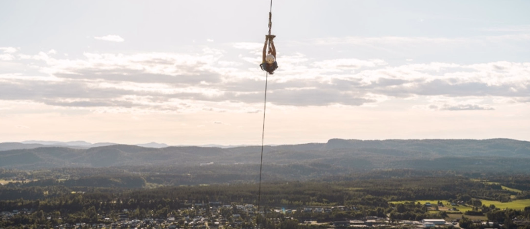 Person i strikkhopp henger opp ned over et landskap med elv og skog